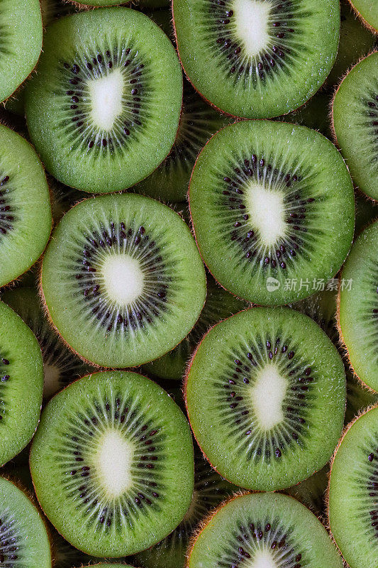 猕猴桃(Actinidia chinensis)切片的全帧图像，中国醋栗显示模糊的棕色皮肤和亮绿色的果肉，黑色的种子环，健康饮食海报壁纸背景设计，高架视图